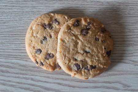 Two cookies with chocolate chips on wooden background