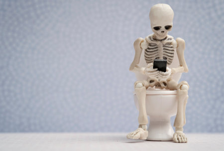Skeleton getting busy with his smartphone while sitting on water closetの写真素材