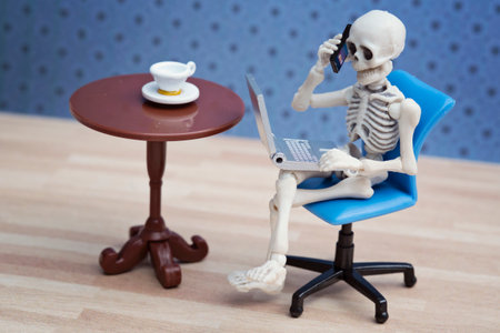 Skeleton calling with laptop on his lapの写真素材