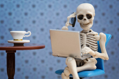 Skeleton calling with laptop on his lapの写真素材