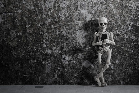 A skeleton leaning on a grungy wall with smartphone in his hand