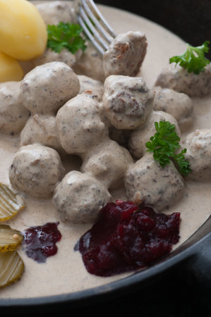 Homemade meatballs in gravy. Served with potato, pickled cucumber and lingonberry jam.の写真素材