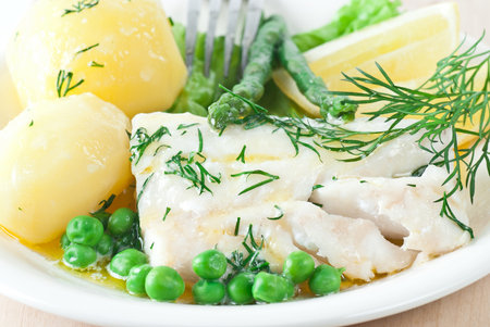 Cooked cod with melted butter and dill. Served with potato and green peas.