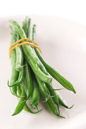 Bunch of rinsed green beans with rubber band on a plate.