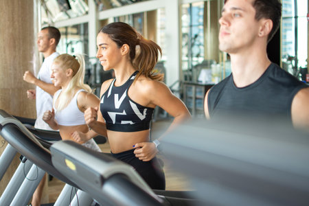 Young people running on a treadmill at gym.