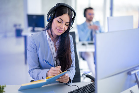 Female telephone operator wearing headset taking notes, communicating with customers and resolving their issues.の写真素材