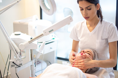 Therapist applying curative facial cheeks massage to young woman in beauty salon.の写真素材