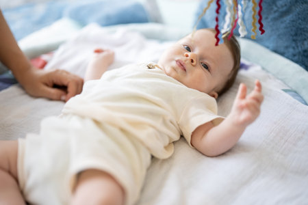 Adorable little baby lying on children rug looking up and playing with toys.の写真素材