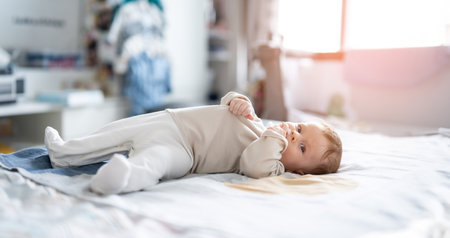 Adorable little boy lying on a bed with hands in his mouth.の写真素材