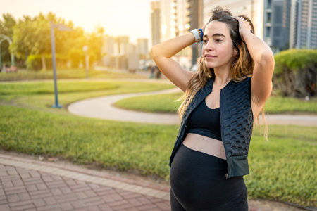 Portrait of beautiful young pregnant woman with hands on head enjoying calm sunset in the parkの写真素材