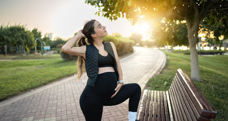 Young pregnant woman in sportswear enjoying her pregnancy in the park at sunset.