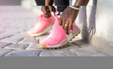 Closeup of black womans hands tying the laces of her running shoes, getting ready for a jog on the...