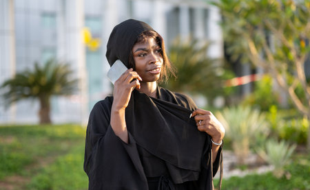 Portrait of young African muslim woman wearing abaya talking on phone outdoors.の写真素材