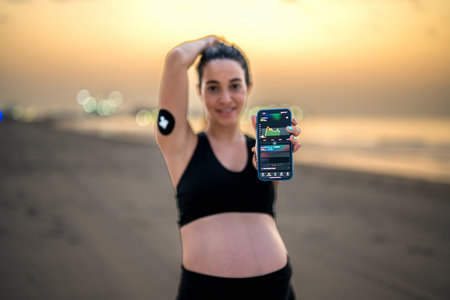 Sporty pregnant woman showing phone displaying blood sugar test on smartphone App.