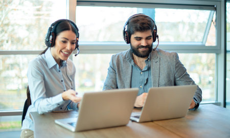 Business man and woman telephone operators with headsets talking to customer on laptop in customer service helpline.の写真素材