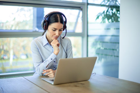 Concentrated business woman helpdesk operator using laptop at modern office.の写真素材
