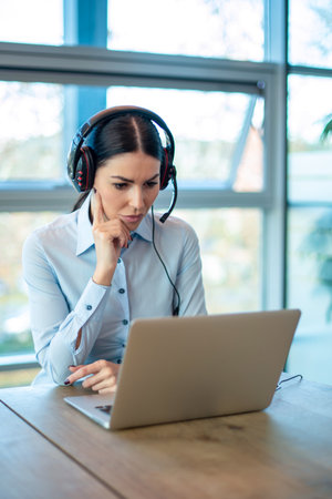 Female consultant of call center in headphones working on laptop at office.