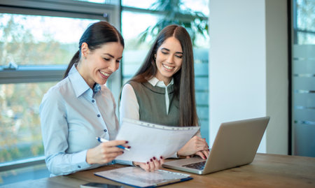 Smiling female business coworkers discussing a paper document at office.の写真素材