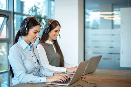Two female support service operators with headset and laptops assisting customers during phone calls...
