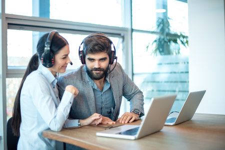 Two business colleagues with headset and laptop chatting at office.の写真素材