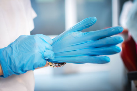 Close up of female doctors hands putting on blue sterilized surgical gloves in the office
