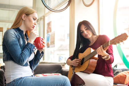 Young female listening while her girlfriend playing guitar at a cafeの写真素材
