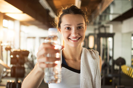 Smiling young woman holding bottle with water in gym.の写真素材