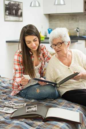 Granddaughter and her grandmother sitting on couch and ad looking at old pictures at homeの写真素材
