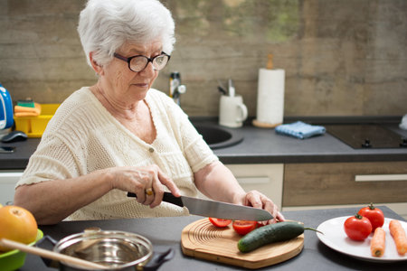 Senior woman preparing healthy food from fresh vegetables in kitchenの写真素材