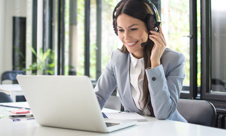 Smiling female customer support operator talking with client and using laptop in office.の写真素材