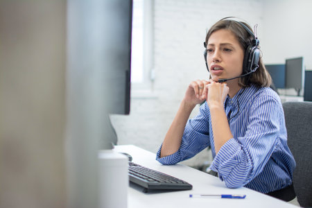 Beautiful young call centre telephone worker talking with a client while sitting bellow computer.の写真素材