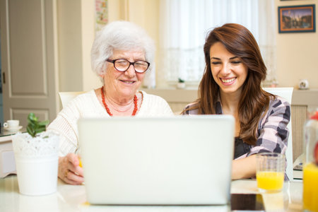 Granddaughter and her grandmother using laptop together at home.