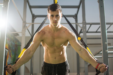Young handsome shirtless man exercising with fitness straps in the outdoor gym.の写真素材