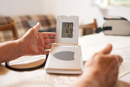 Close up of senior womans hands measuring blood pressure with digital blood pressure monitor.