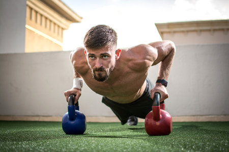 Portrait of a muscular man doing push ups with kettle bells in gym.