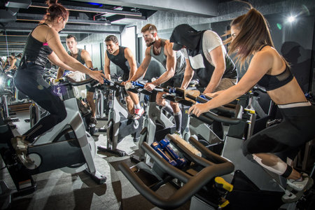 Group of fitness people doing cardio workout on indoor cycling bikes at gym.