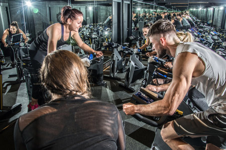 Group of young people having cycling class with their female instructor at gym.