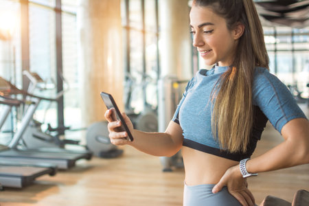 Fitness woman using phone at the gym. Sporty girl taking break from working out and reading message...
