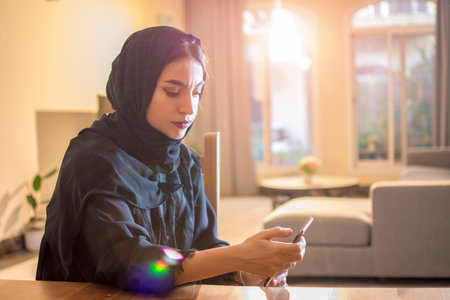 Beautiful muslim woman wearing hijab using smart phone while sitting at home.の写真素材