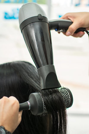 Drying long black hair with hair dryer and round brush. Close-up.の写真素材