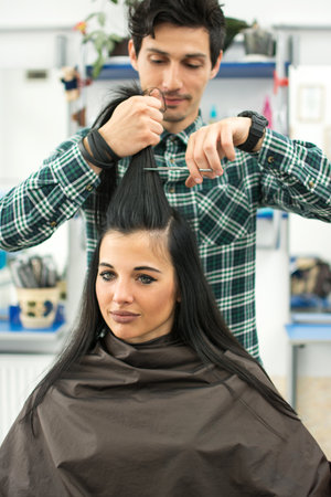 Young male hairdresser cutting clients hair with scissors at hair salon.の写真素材
