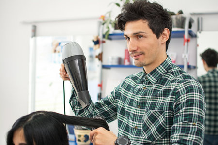 Male hairdresser using hairbrush and hair dryer at hair salon.の写真素材