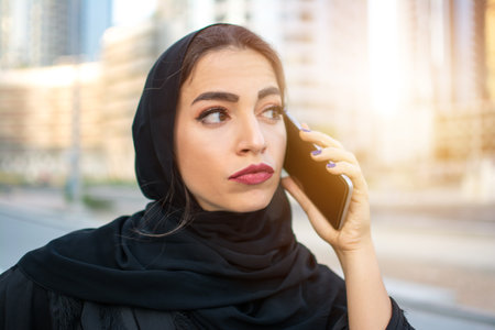 Arab businesswoman wearing Abaya traditional clothing talking on smart mobile phone on the street