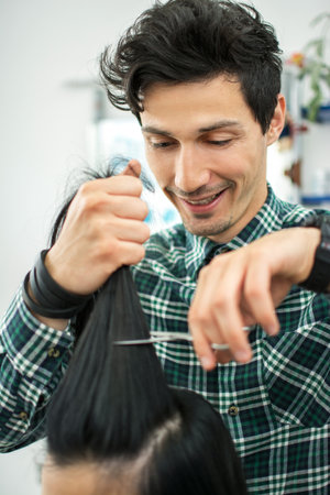 Young male hairdresser cutting clients hair with scissors at hair salon.の写真素材