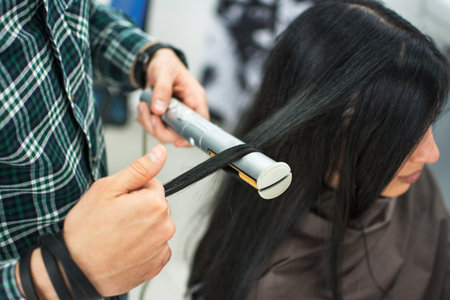 Close up of a hairdresser straightening long black hair with hair irons.の写真素材