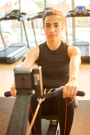 Fit young woman working out on a rowing machine at the gym. Caucasian female doing cardio exercise...