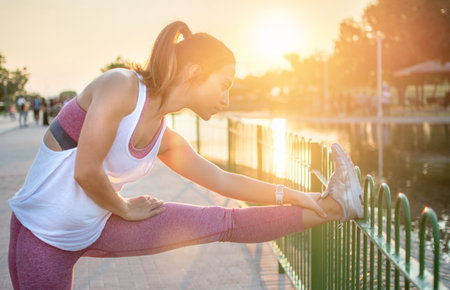 Beutiful female runner doing stretching exercise before running outdoors