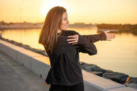 Portrait of beautiful young woman stretching arms before running outside. Smiling woman warming up before running.の写真素材