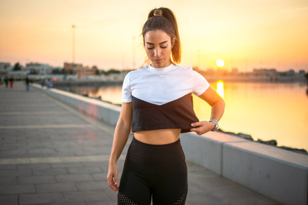 Serious young fitness woman standing on sidewalk wearing sportswear at sunset outdoors