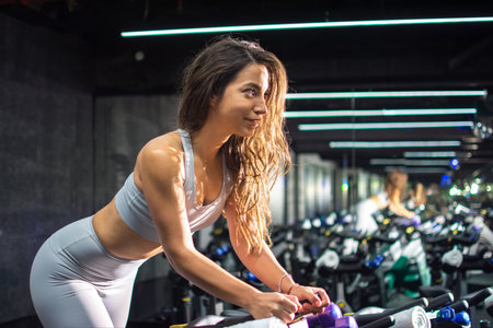 Side view profile on beautiful young woman riding on the spinning bike at gymの写真素材